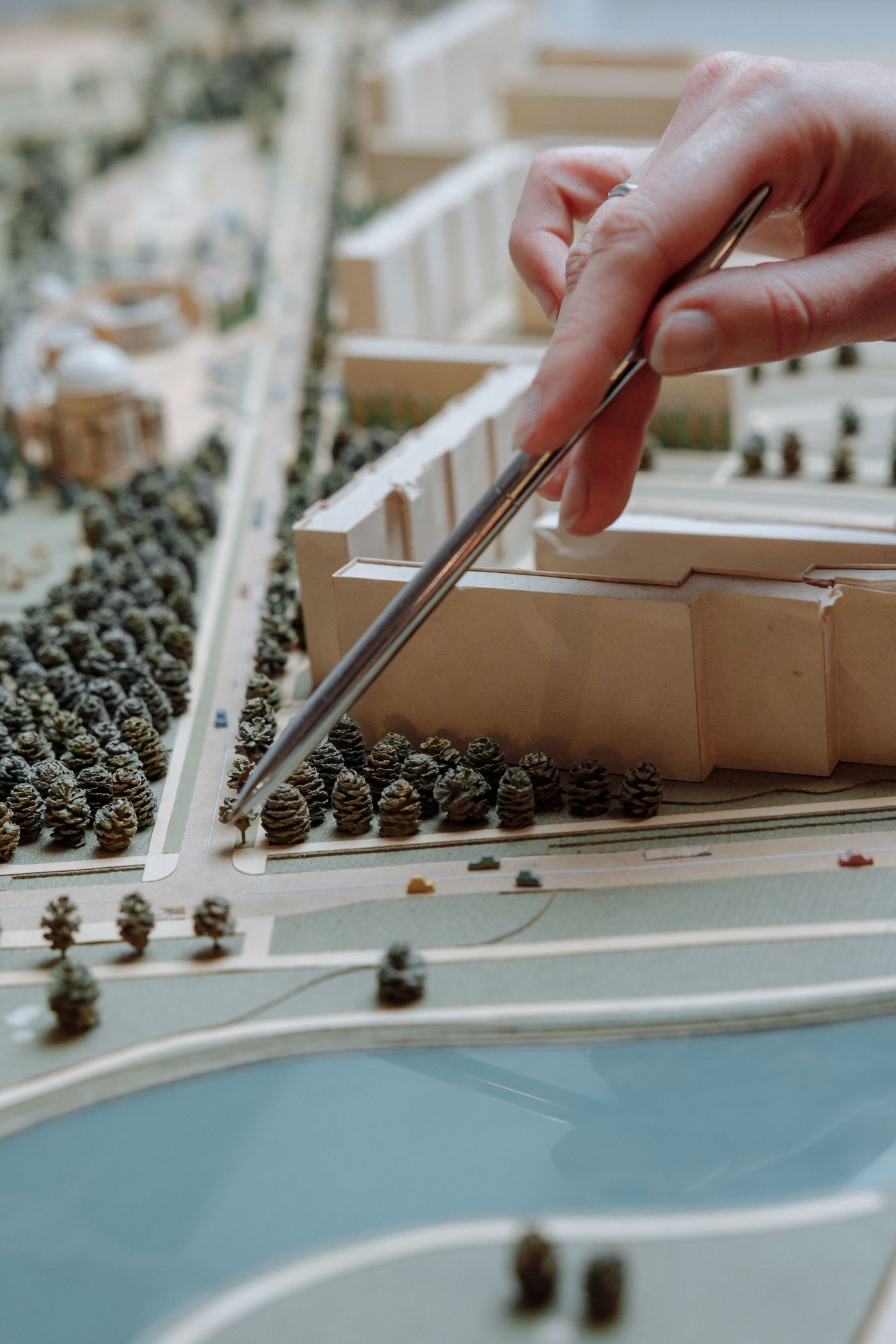 A hand places trees on a detailed architectural site model during project planning.